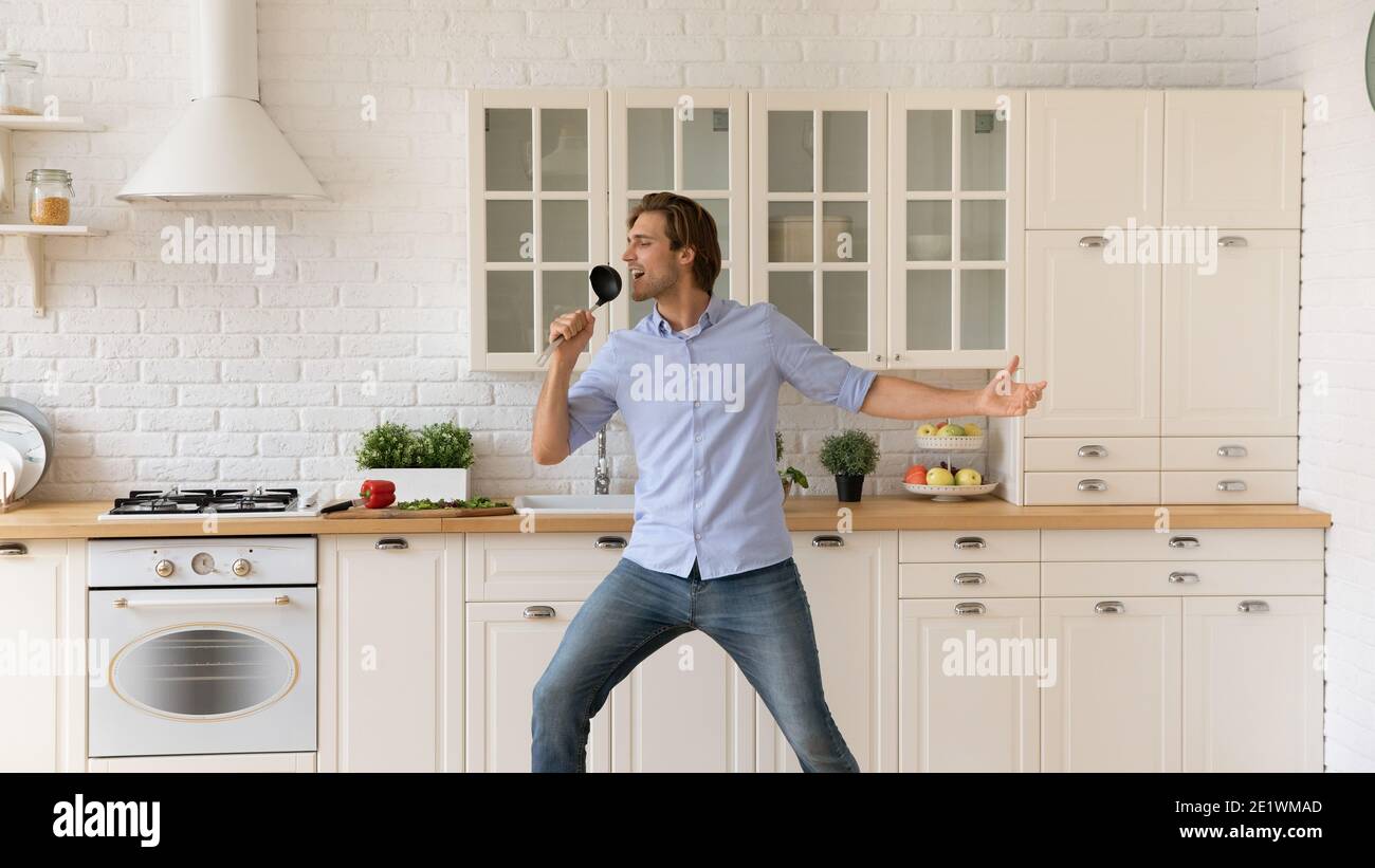 Il giovane sorridente si diverte a cucinare ballando in cucina Foto Stock