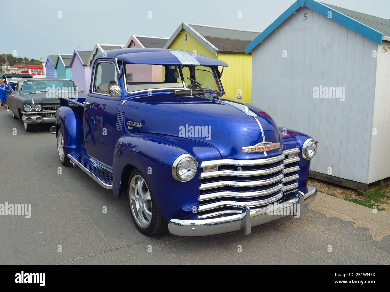 Classic Blue Chevrolet 3100 pick-up camion sul lungomare di fronte a capanne sulla spiaggia. Foto Stock