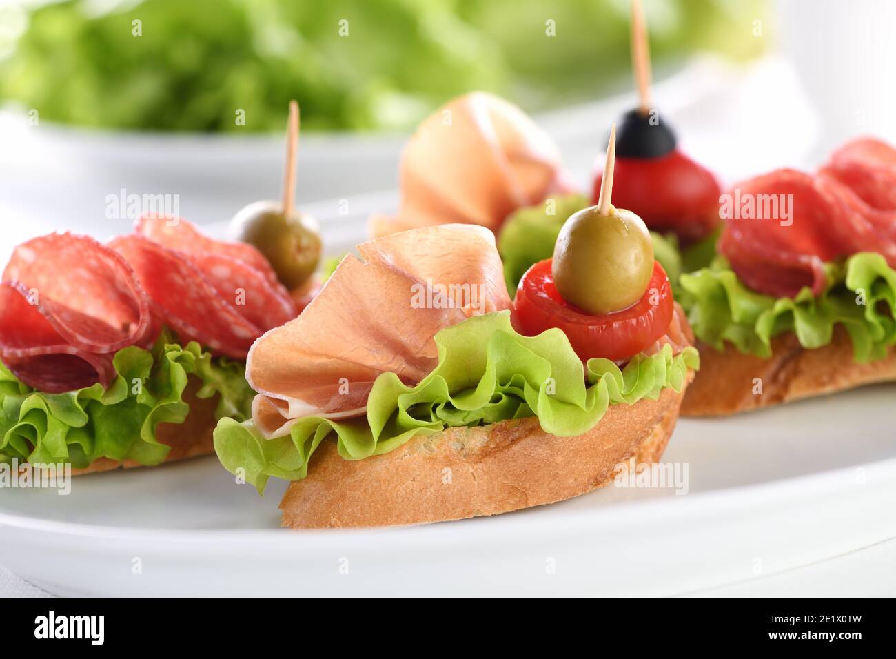 Tartine di baguette tenue con lattuga, salame o prosciutto di Parma, pomodori, mozzarella e olive. Piatto assortito di prelibatezze per la festa. Foto Stock