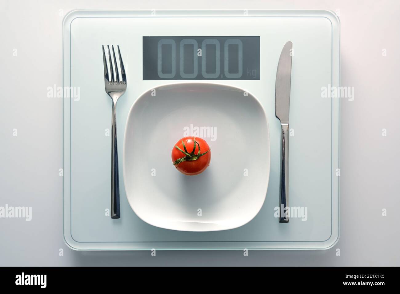 Pomodoro su un piatto bianco e posate su una scala di peso personale che mostra zero, dieta sana e concetto di dimagrimento, spazio di copia, vista ad angolo alto dall'alto Foto Stock