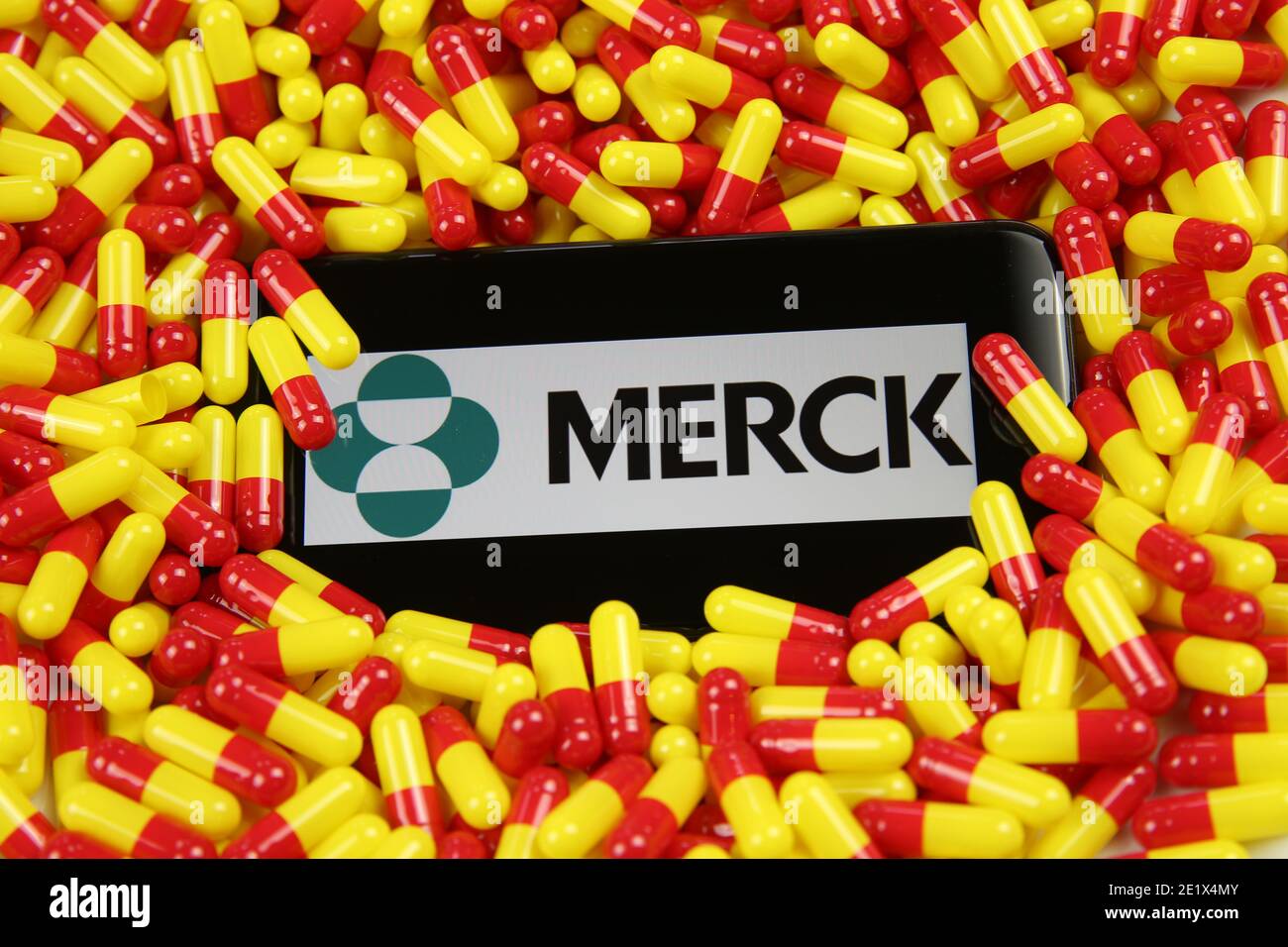 Viersen, Germania - 9 aprile. 2020: Primo piano dello schermo del telefono cellulare con la scritta del logo della società farmaceutica Merck su capsule di farmaco rosse in pile gialle Foto Stock