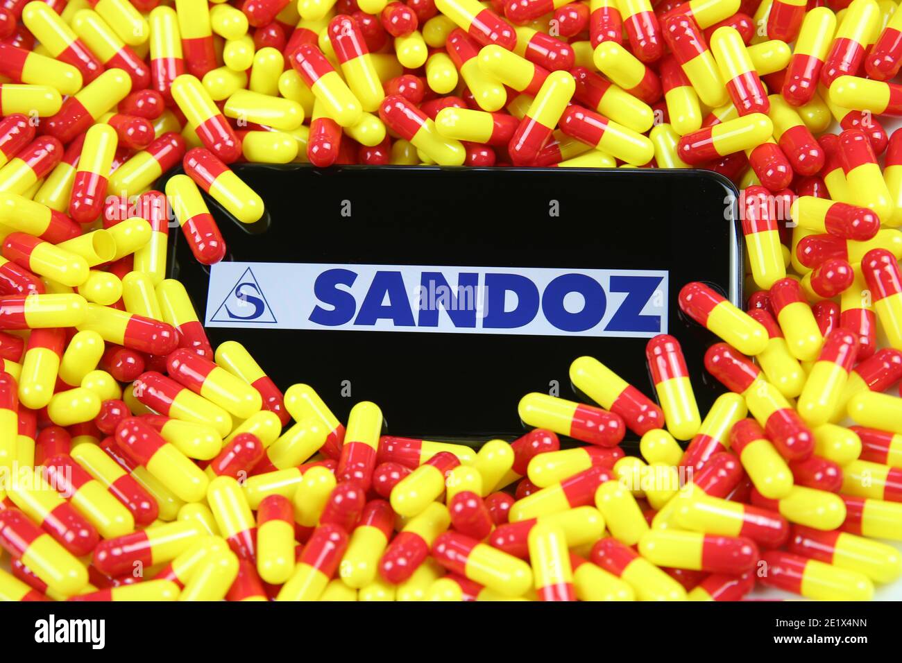 Viersen, Germania - 9 aprile. 2020: Primo piano dello schermo del telefono cellulare con la scritta del logo della società farmaceutica Sandoz sulla capsula di farmaco rosso palo giallo Foto Stock