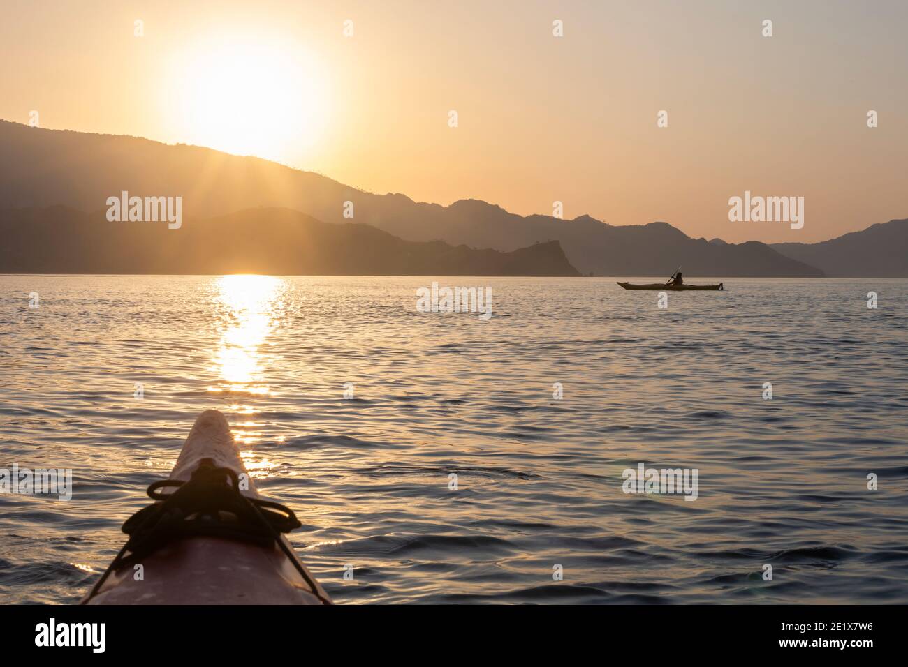 silhouette di un kayak nell'oceano al tramonto con di kayak irriconoscibile e una catena montuosa sullo sfondo Foto Stock