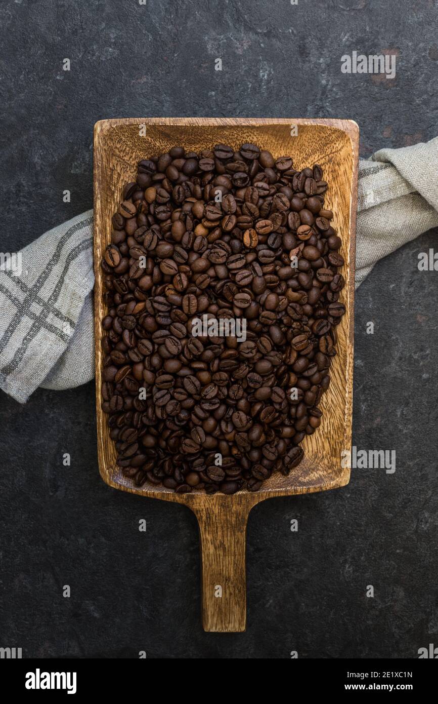 Pala in legno piena di chicchi di caffè tostati su fondo di pietra scuro. Foto Stock
