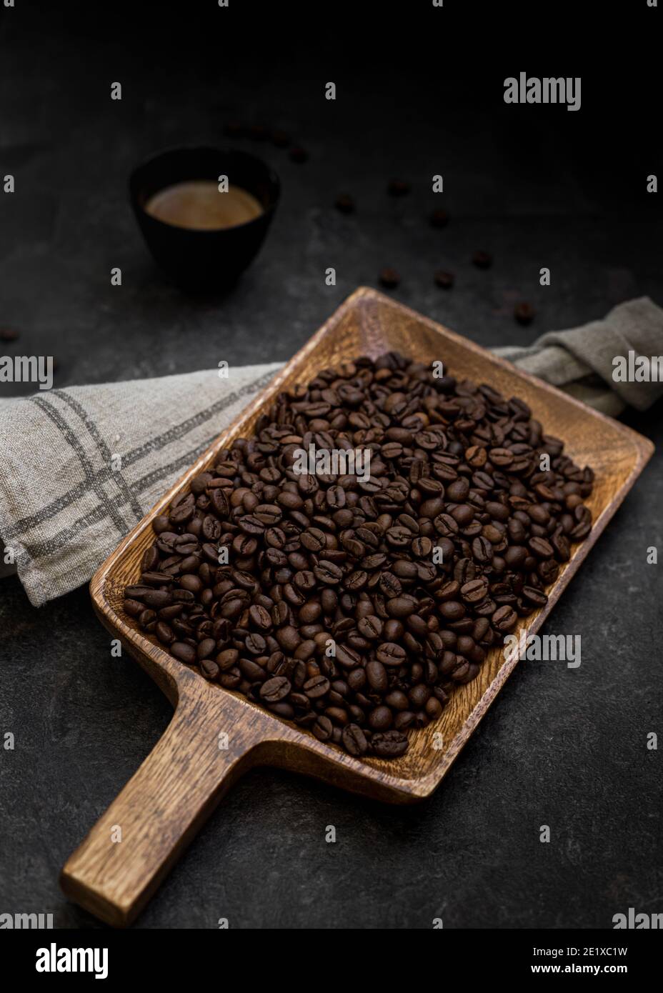 Vista inclinata di una pala in legno con una grande quantità di chicchi di caffè tostati sopra di essa. Uno sfondo di pietra con alcuni chicchi di caffè isolati e un co Foto Stock