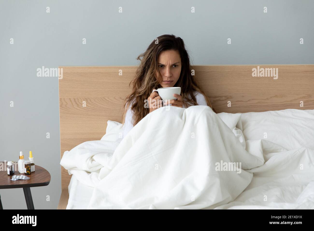 Donna infelice che sente di tenere una tazza di tè, seduto a letto Foto Stock