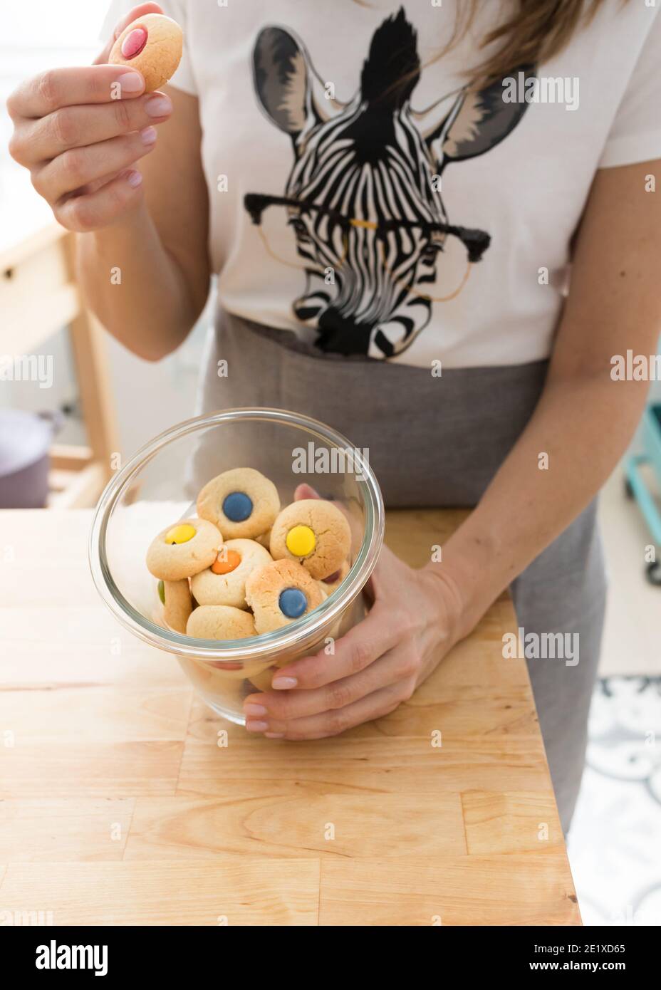 Donna vestita con una t-shirt zebra che raccoglie un biscotto rosso con la mano destra e mostra un vaso aperto pieno di biscotti colorati. Foto Stock