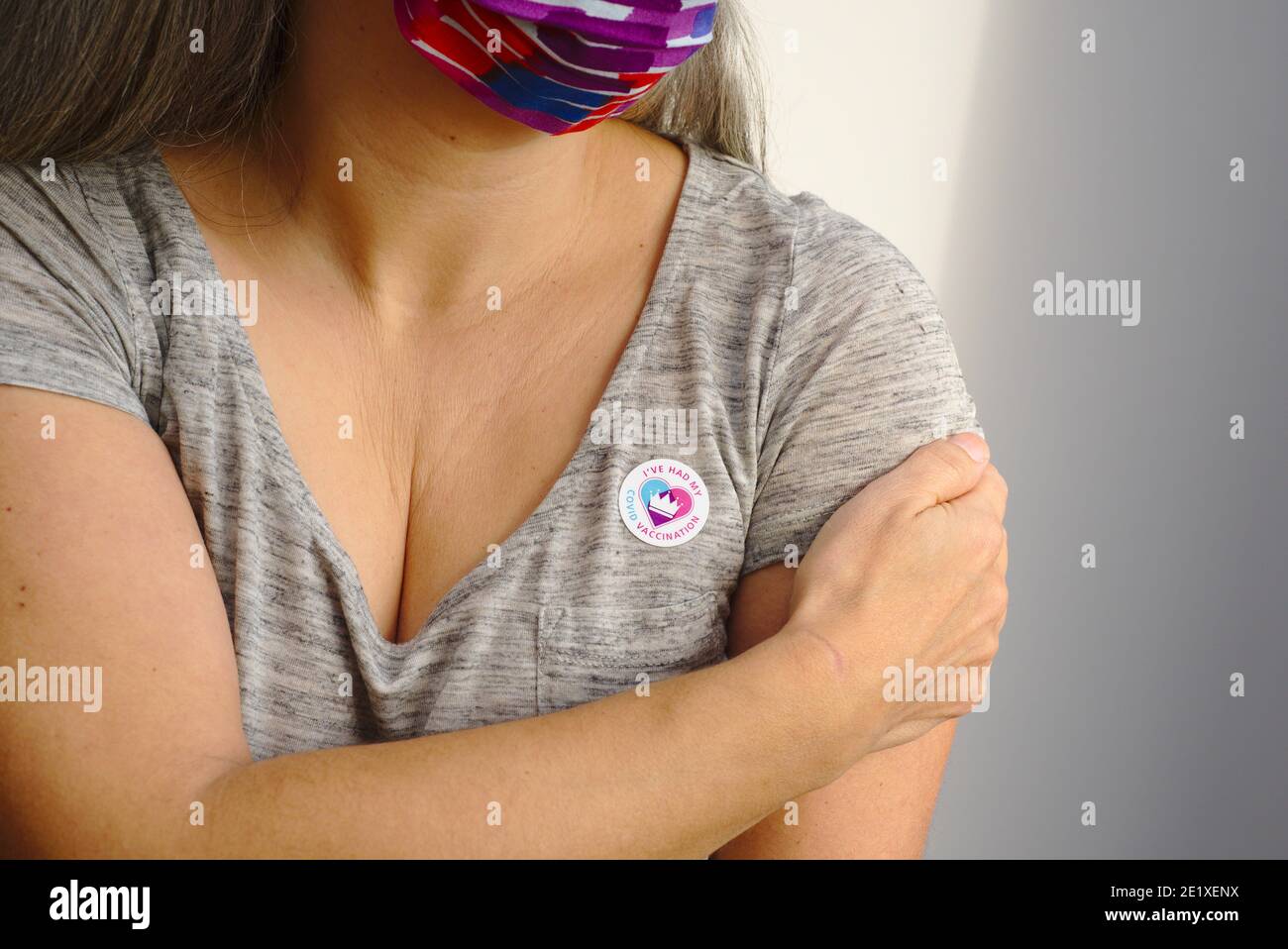 Donna che indossa una maschera facciale che tiene il braccio dopo aver ricevuto il vaccino Covid19 nel Regno Unito. Ha un adesivo che dice che ho avuto la mia vaccinazione Covid. Foto Stock