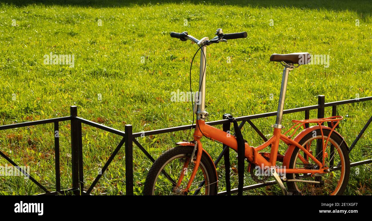Bicicletta compatta da città a piedi su sfondo verde con spazio per la copia. Servizio di turismo urbano e noleggio biciclette. Foto Stock
