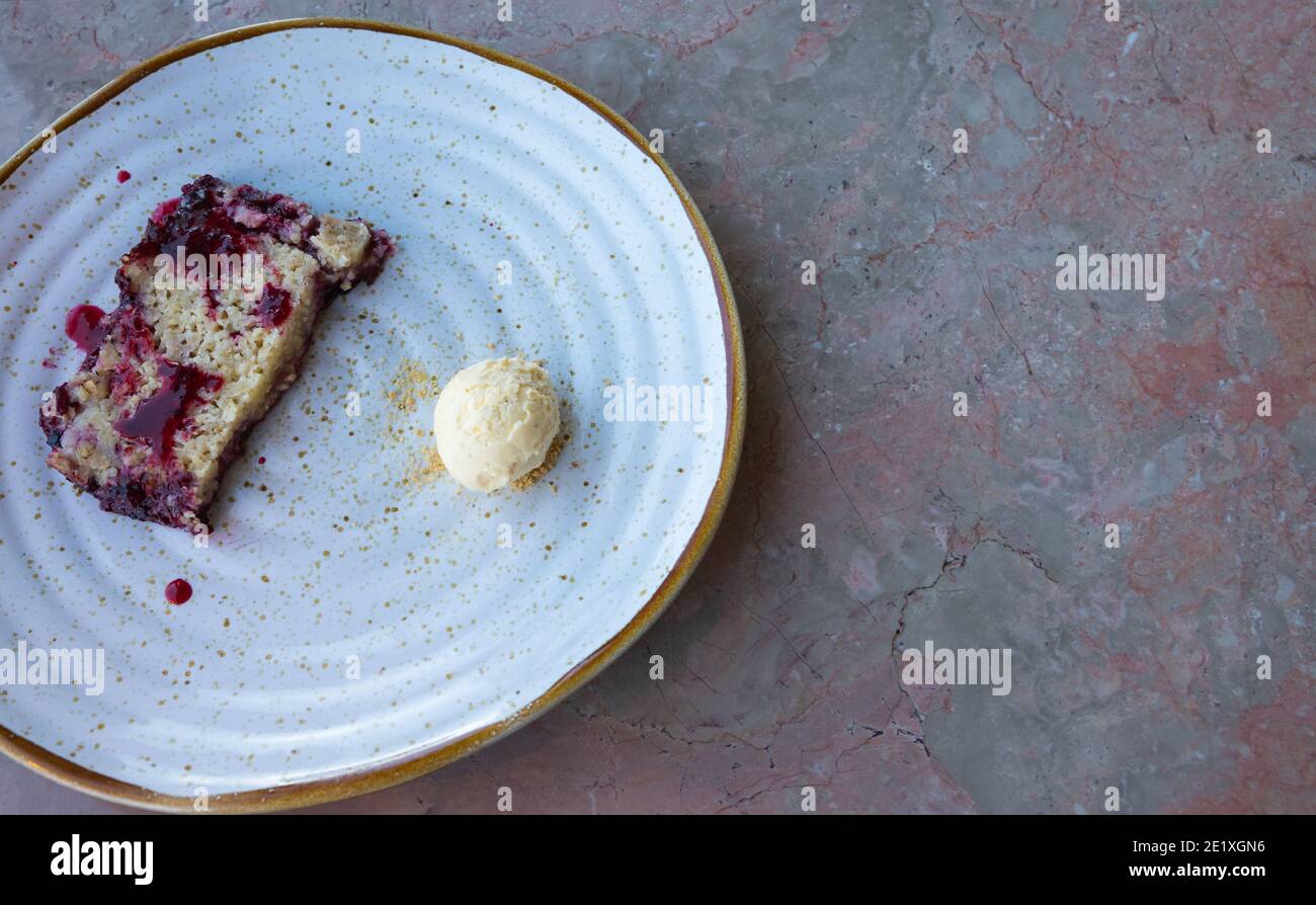 La frutta rossa crumble e un piccolo dessert della sfera del gelato della vaniglia pronto da mangiare su un tavolo di marmo rosa. Spazio di copia sul lato destro. Foto Stock