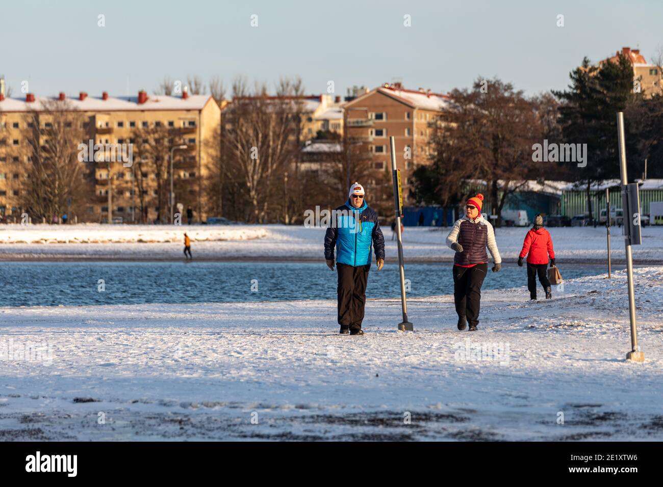 Coppia di mezza età con una passeggiata sulla spiaggia innevata di Hietaranta in una soleggiata giornata invernale a Helsinki, Finlandia Foto Stock