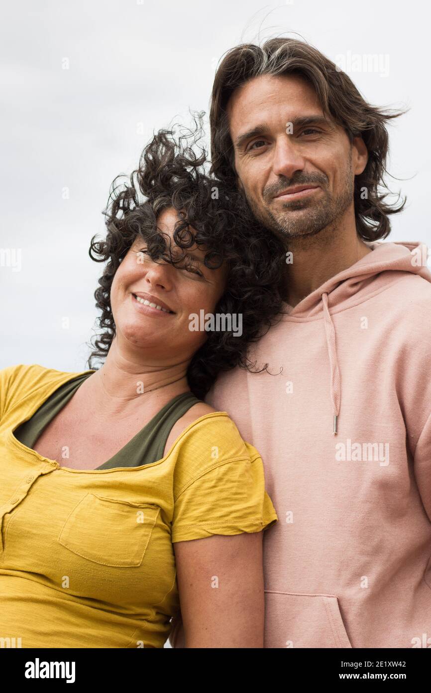 Giovane donna sorridente con capelli ricci e camicie gialle si appoggia sul bel ragazzo alto con capelli lunghi. Bel ritratto di coppia. Abbigliamento casual Foto Stock