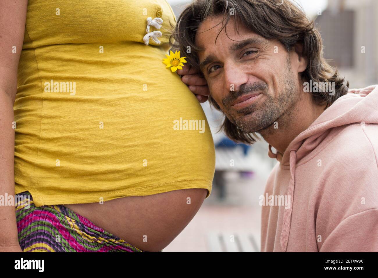 Orgoglioso papà appoggia la testa sulla madre incinta che detiene il fiore giallo. Un padre entusiasta in attesa di un nuovo membro della famiglia. Aspettandosi genitori, la salute delle donne Foto Stock