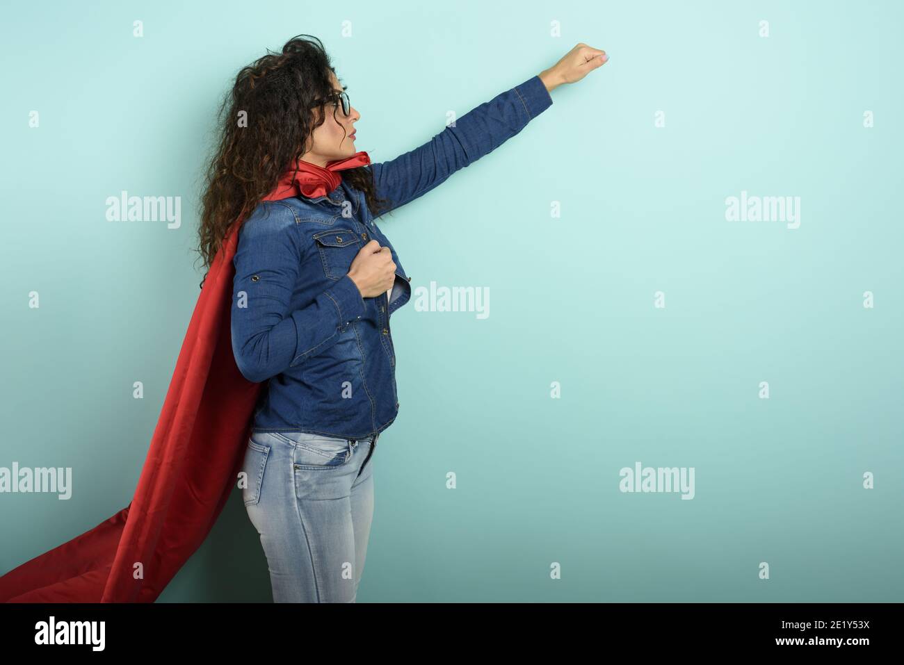 La donna agisce come un supereroe. Concetto di determinazione e potenza. Sfondo ciano Foto Stock