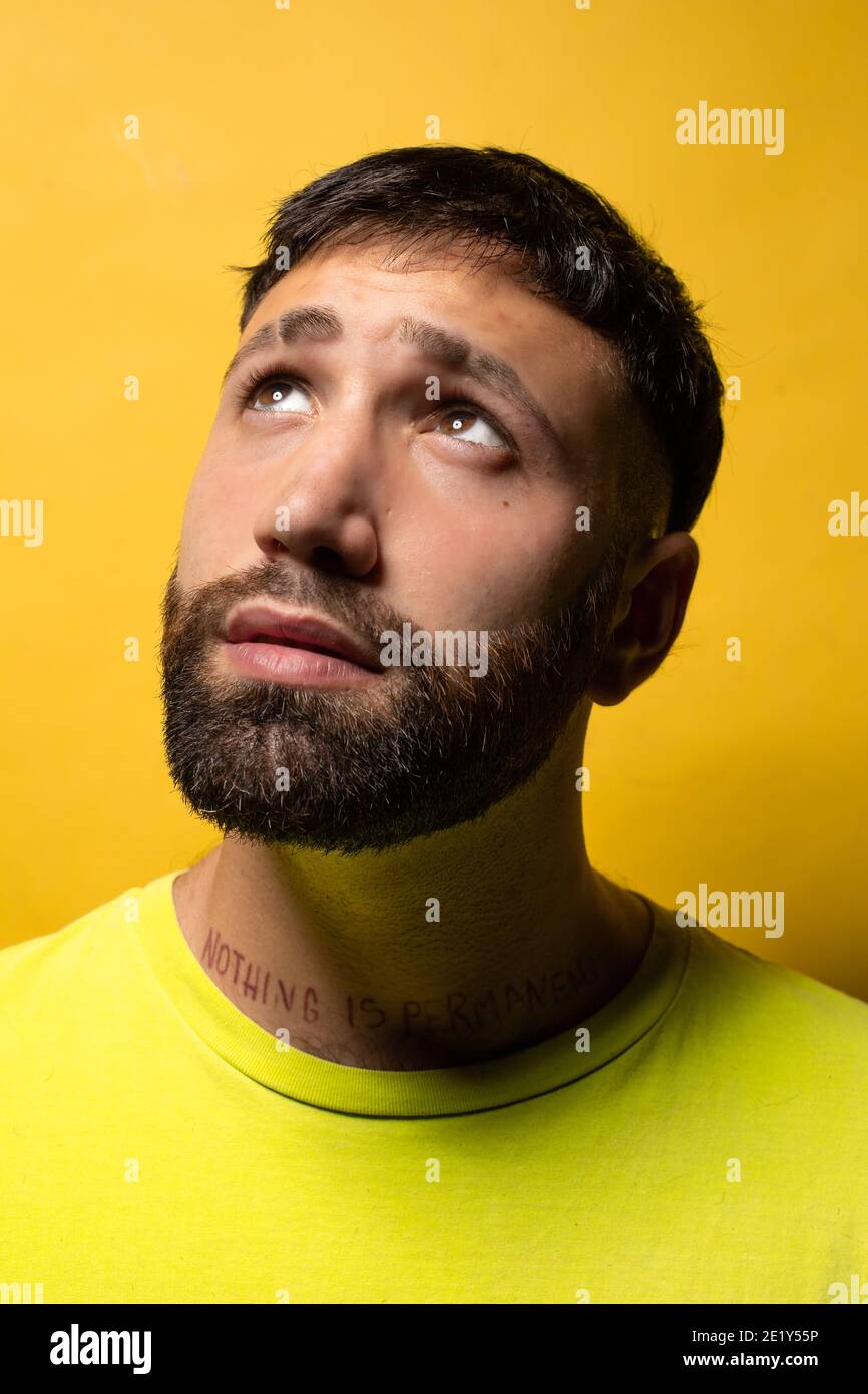 Ritratto di un giovane con barba e maglietta gialla su sfondo giallo guardando in su interessato Foto Stock