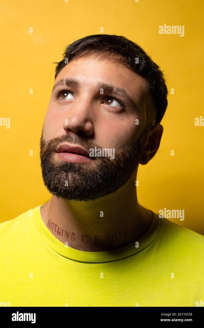 Ritratto di giovane sorridente con barba e maglietta gialla su sfondo giallo guardando verso l'alto Foto Stock