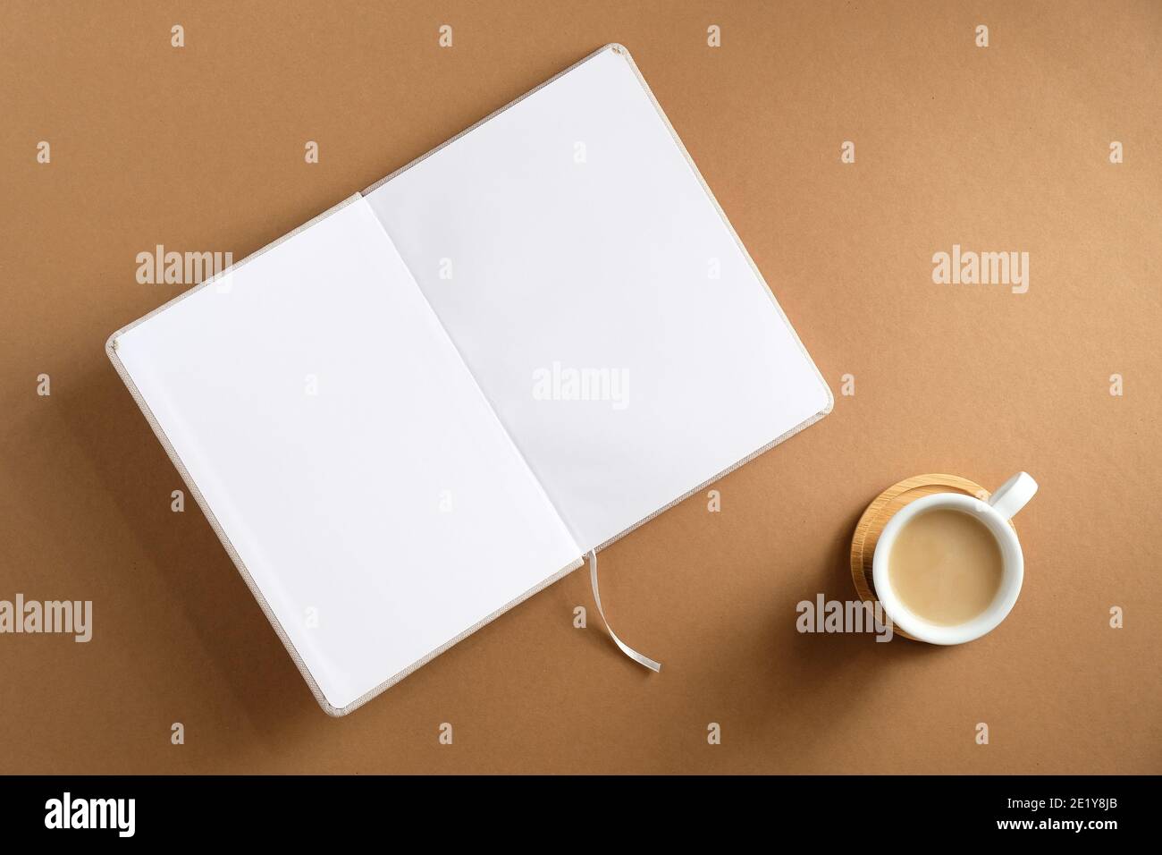 Aprì un libro vuoto e una tazza di caffè su sfondo marrone. Disposizione piatta, vista dall'alto. Accogliente scrivania da ufficio. Foto Stock