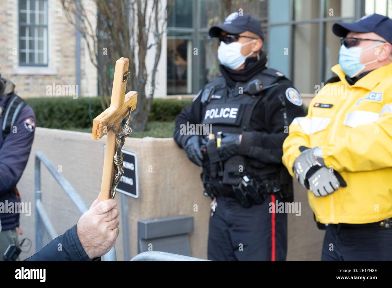 In risposta alla fing dei churchgoers, un cappellano tiene una croce fuori alla polizia ad una protesta contro i bloccaggi COVID-19 a Toronto, Ontario. Foto Stock