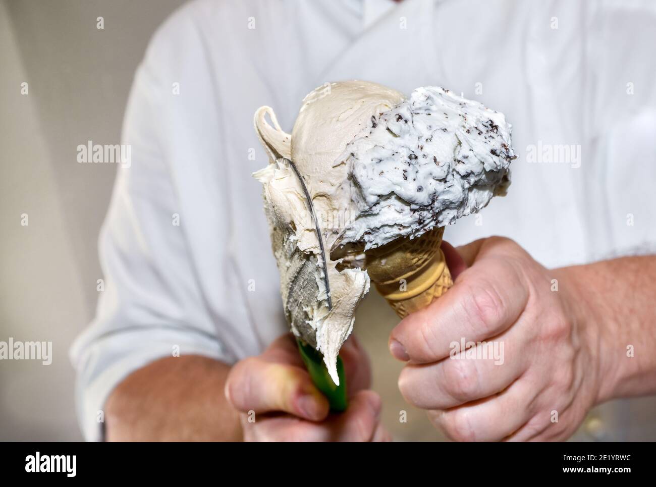Mani della gelatiera mettendo il gelato nel cono del waffle, crema e sapori di stracciatella di cioccolato Foto Stock