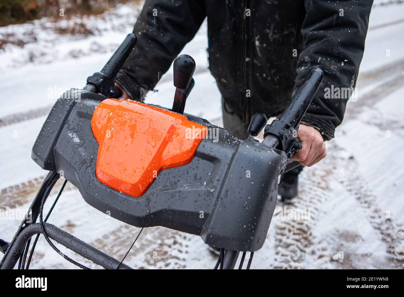 Primo piano di due mani maschili senza guanti che tengono il manubrio di un aratro da neve arancione brillante. Attività di spazzaneve in una fredda giornata invernale. Foto Stock