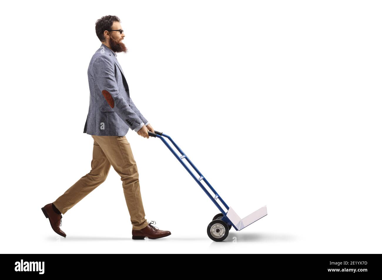 Foto di profilo di lunghezza completa di un uomo bearded che cammina e. spingere un carrello manuale vuoto isolato su sfondo bianco Foto Stock