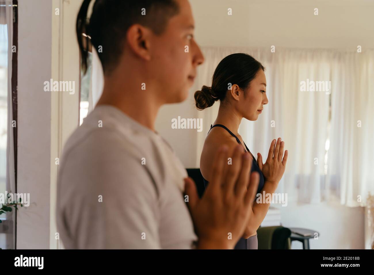 Vista laterale dell'uomo e della donna asiatici che gesturano namaste e. meditare mentre si pratica yoga a casa insieme Foto Stock