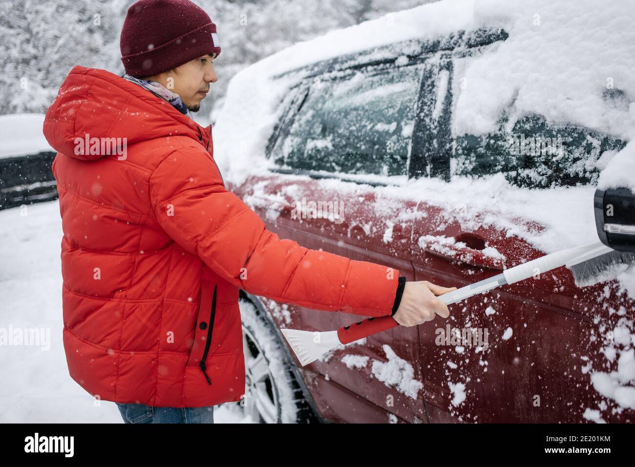 Il ragazzo pulisce l'auto dalla neve con una spazzola. Il concetto di maltempo della neve. Foto Stock