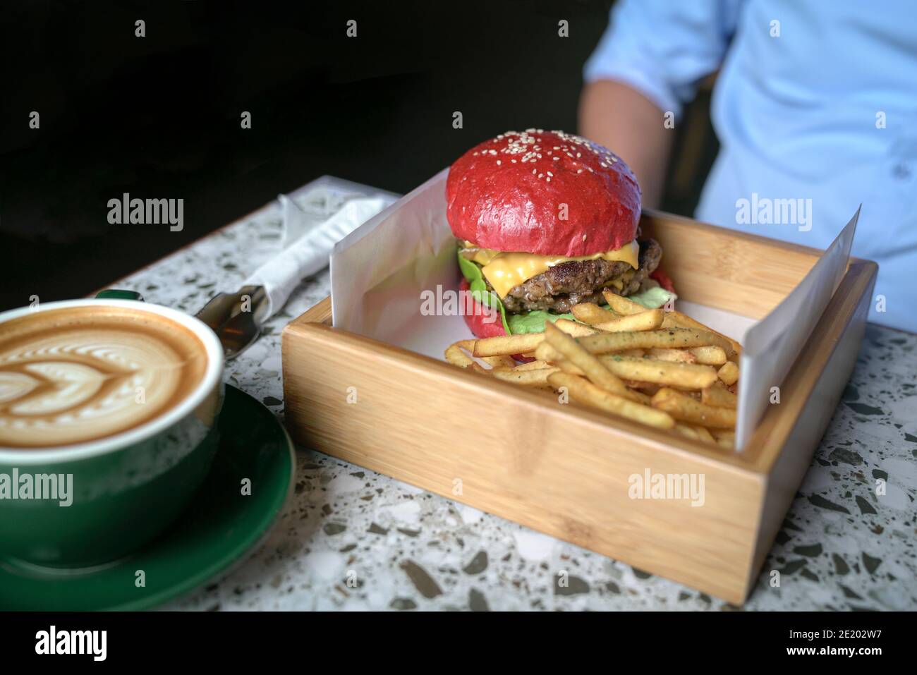 Uomo seduto a un tavolo con hamburger, patatine fritte e caffè. Concetto di tempo di pasto. Foto Stock