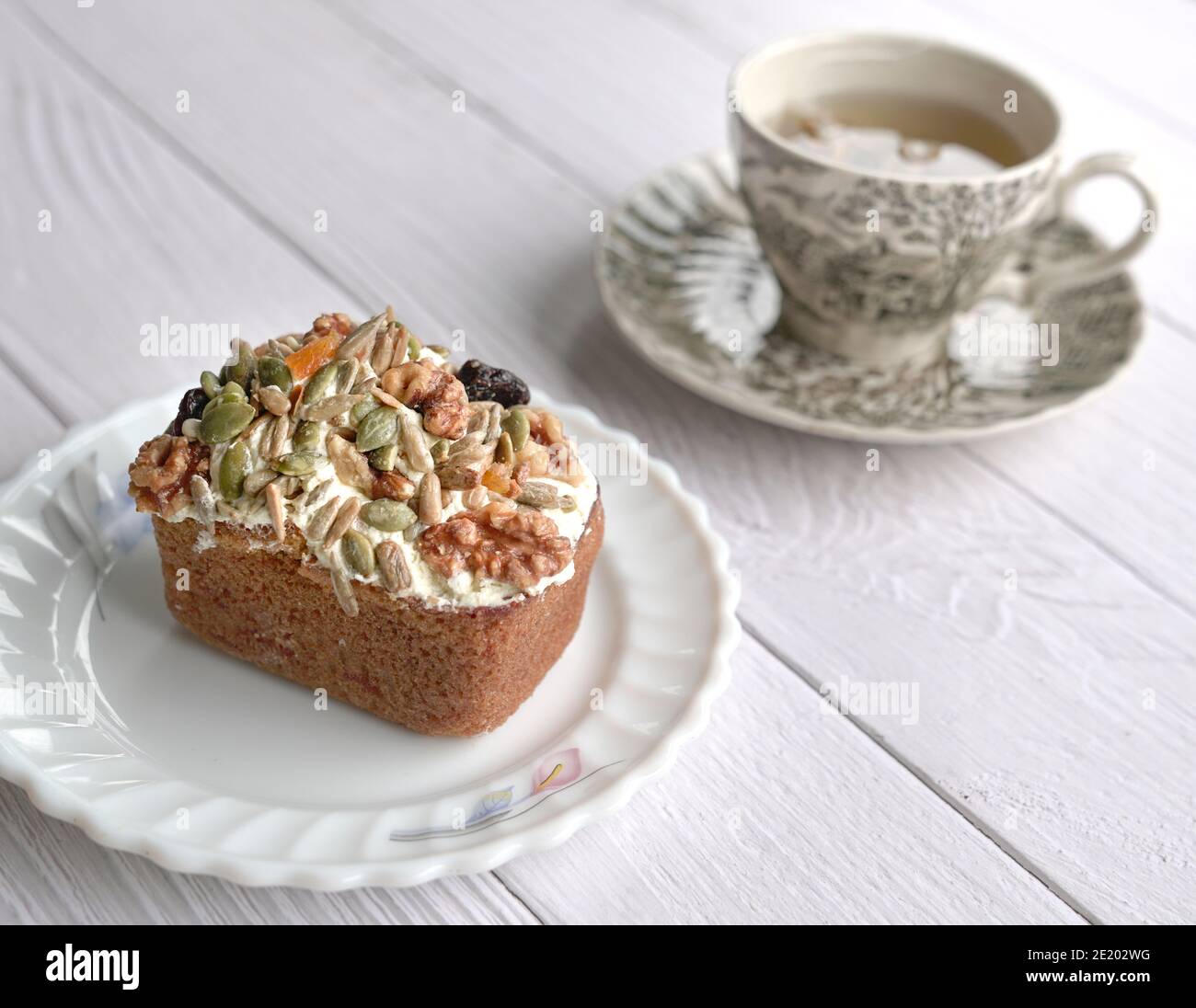Torta di carote con noci miste, semi e frutta secca come farcitura con tazza di tè sullo sfondo. Su tavolo di legno. Foto Stock