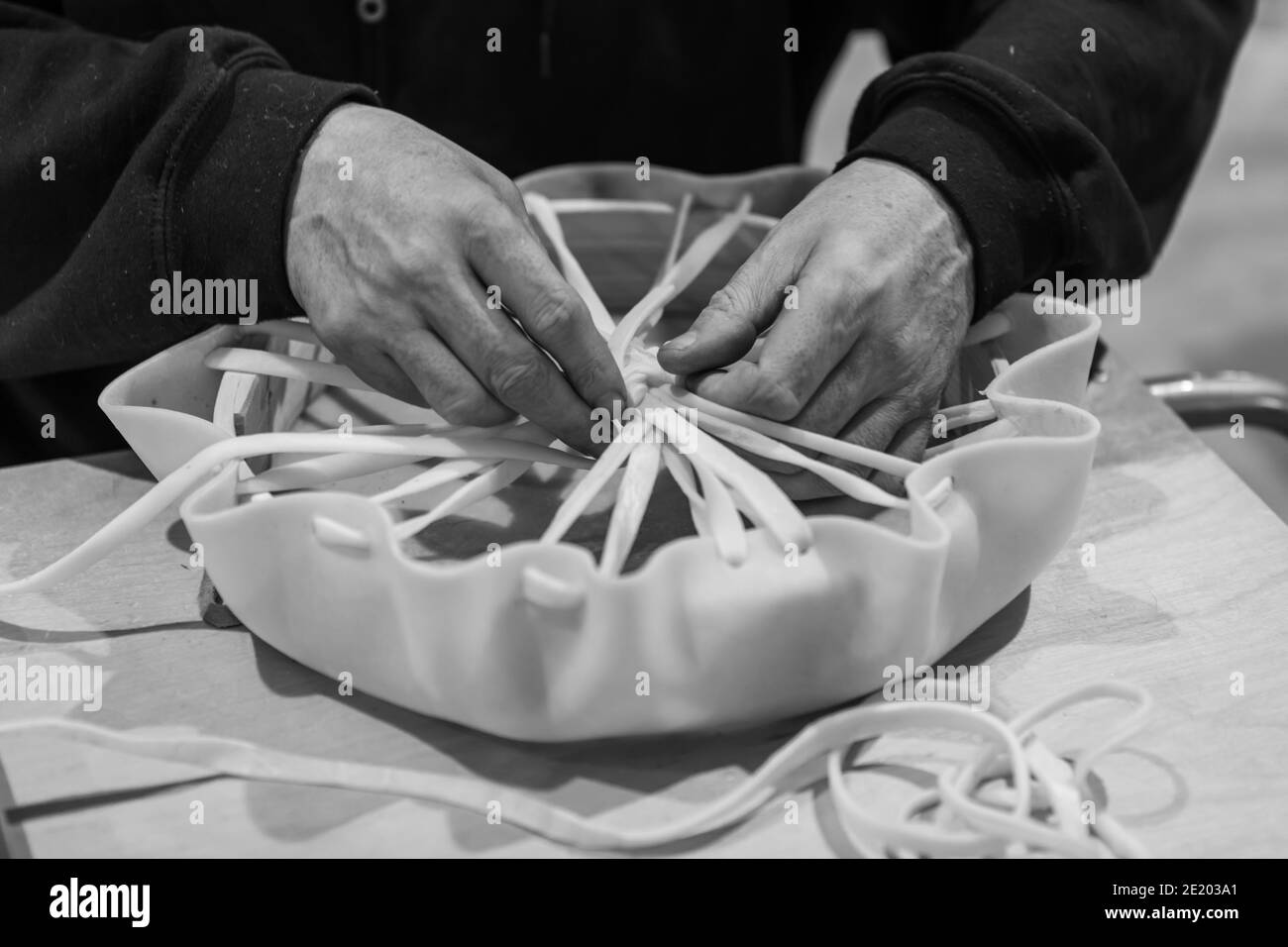 Colpo bianco e nero delle mani dell'uomo che legano le estremità libere di un pezzo di cuoio per generare un tamburello. Momenti di un laboratorio di drum nativo Foto Stock