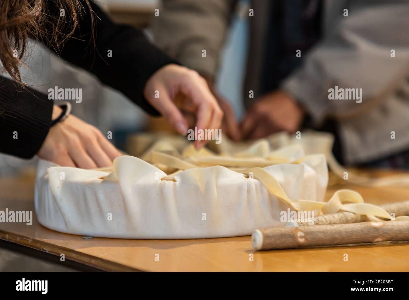 Molto da vicino delle mani della donna che creano un tamburello a mano con un pezzo di pelle, tirando e legando le estremità, durante un laboratorio di tamburo nativo. Foto Stock