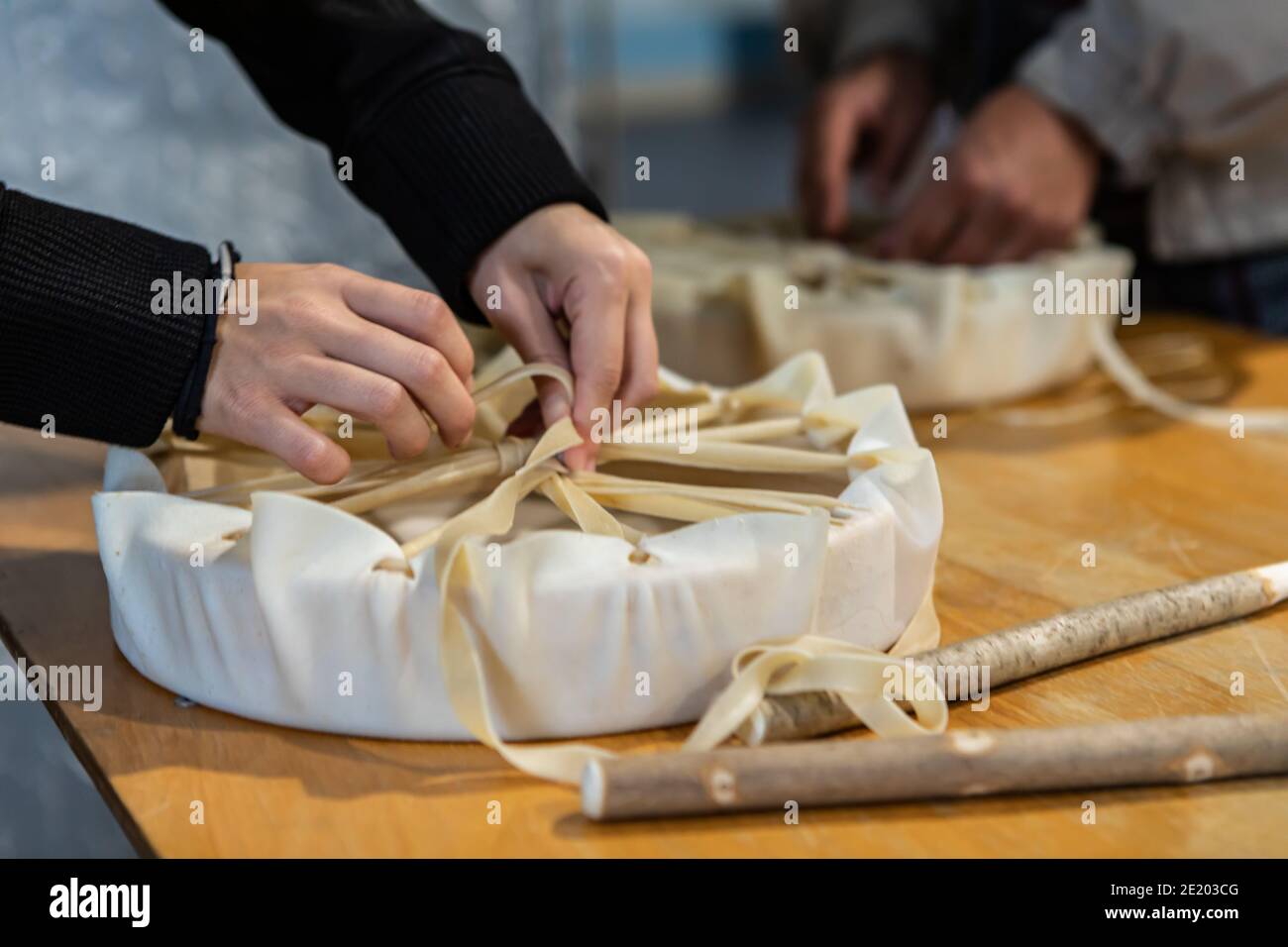 Molto da vicino delle mani della donna che creano un tamburello a mano con un pezzo di pelle, annodandolo finisce l'uno con l'altro durante un laboratorio di tamburo nativo Foto Stock