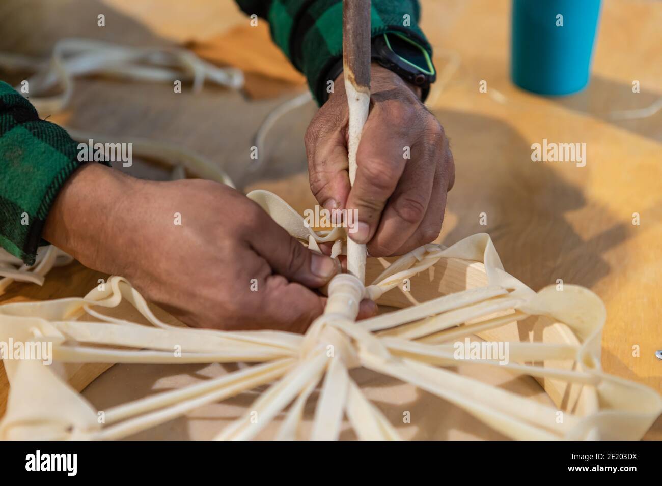 Primo piano delle mani dell'uomo che legano le estremità sciolte di un pezzo di pelle intorno ad un supporto di legno per creare un tamburello. Momenti di un laboratorio di drum nativo Foto Stock