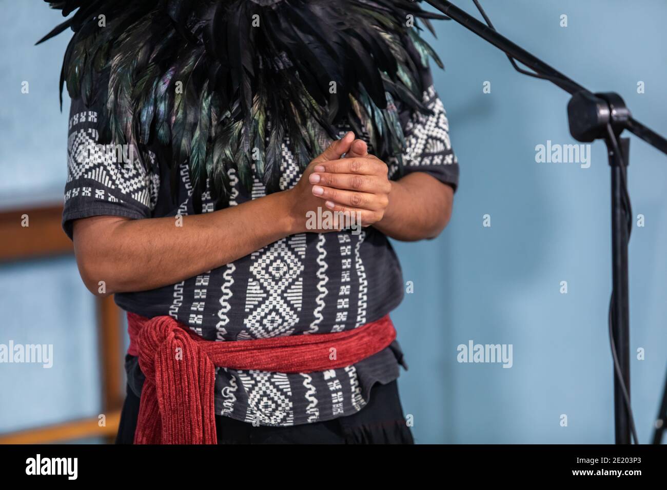 Momenti di un laboratorio di drum nativo. Uomo con decorazioni tradizionali native o indiane fatte con piume che parlano di fronte al microfono. Foto Stock