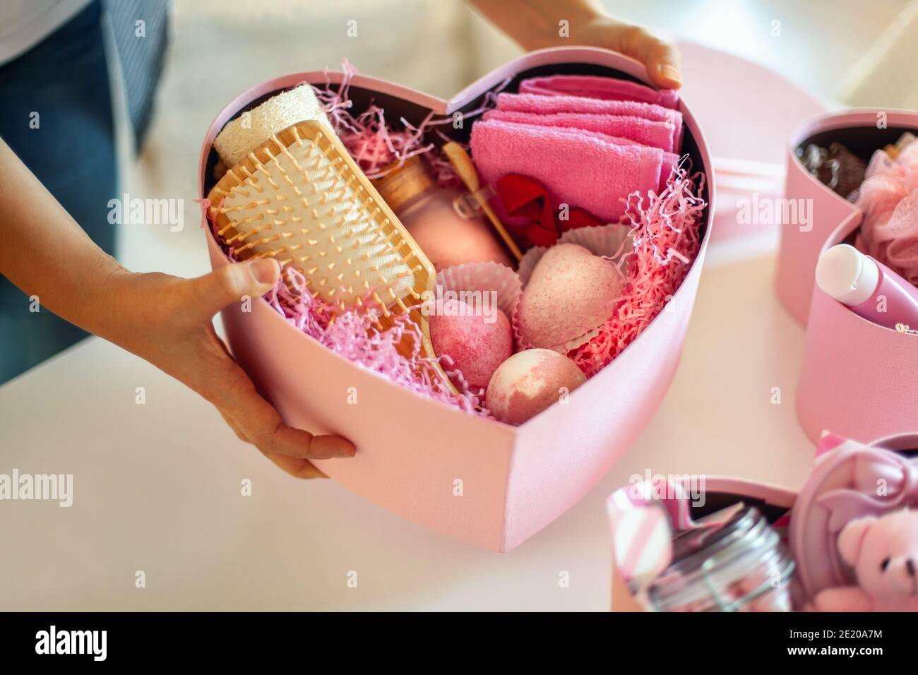 Mani donna che tengono scatole regalo a forma di cuore di colore rosa di prodotti da bagno e corpo per bridesmaids. Foto Stock