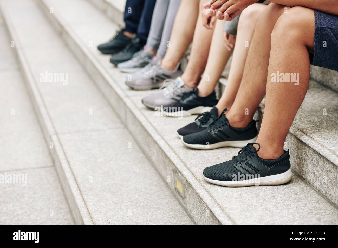 Immagine ritagliata di persone sportive in pantaloncini e sneakers seduti su passaggi dopo l'allenamento all'aperto Foto Stock