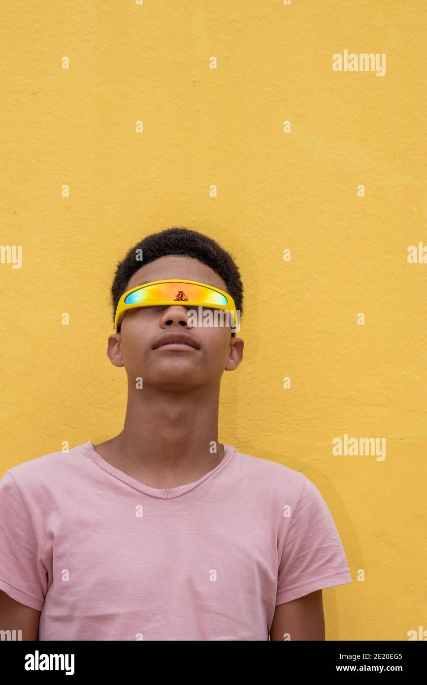 Primo piano di un adolescente contro la parete gialla con futuristico occhiali Foto Stock