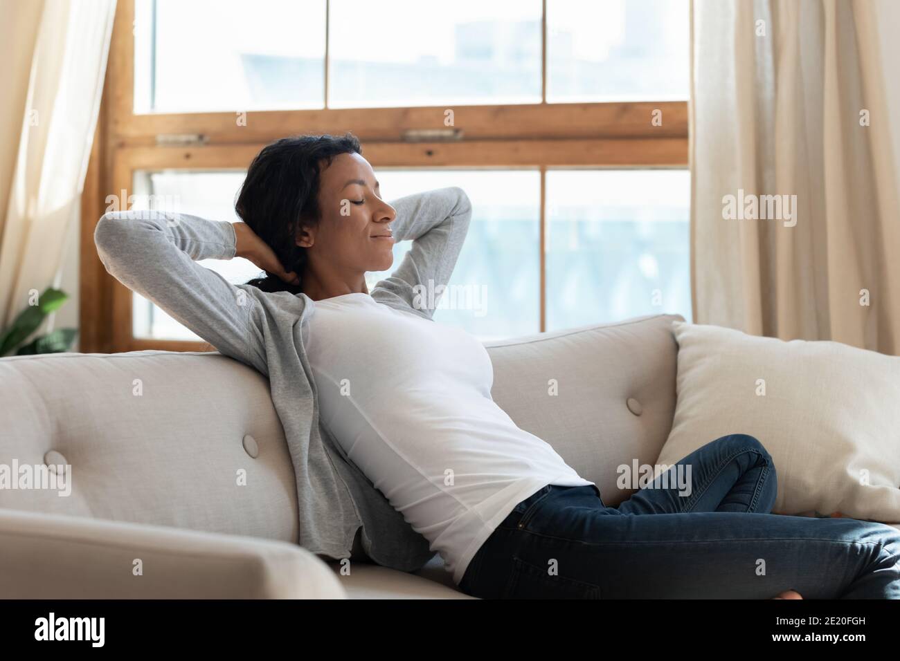 Tranquilla giovane donna biraciale afroamericana che si rilassa su un comodo divano. Foto Stock
