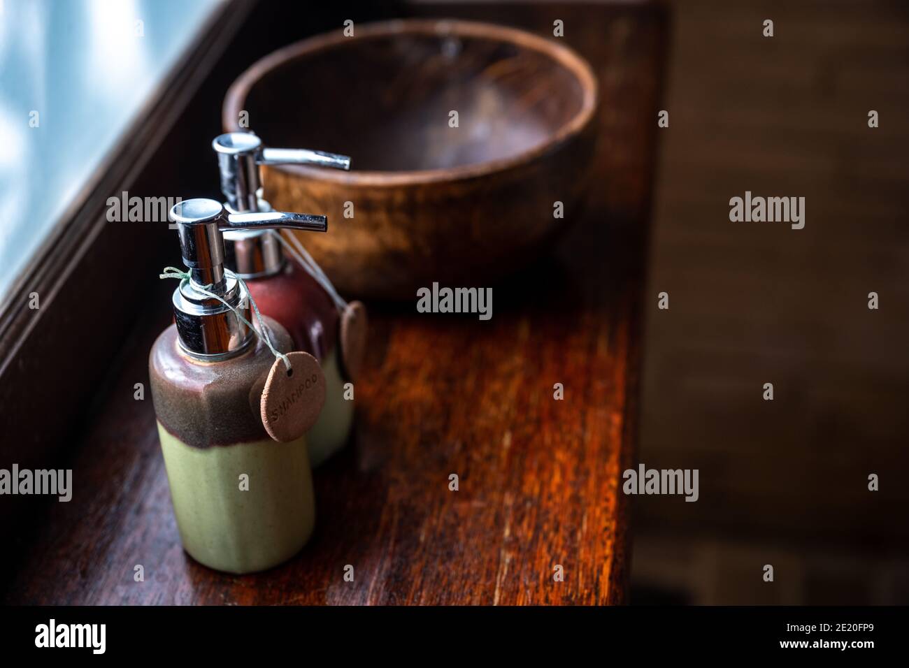 Bottiglie in ceramica di shampoo e gel doccia sono poste in un grande recipiente di legno. E mettere sul banco di legno di vetro satinato sfondo concetto Thai spa f Foto Stock