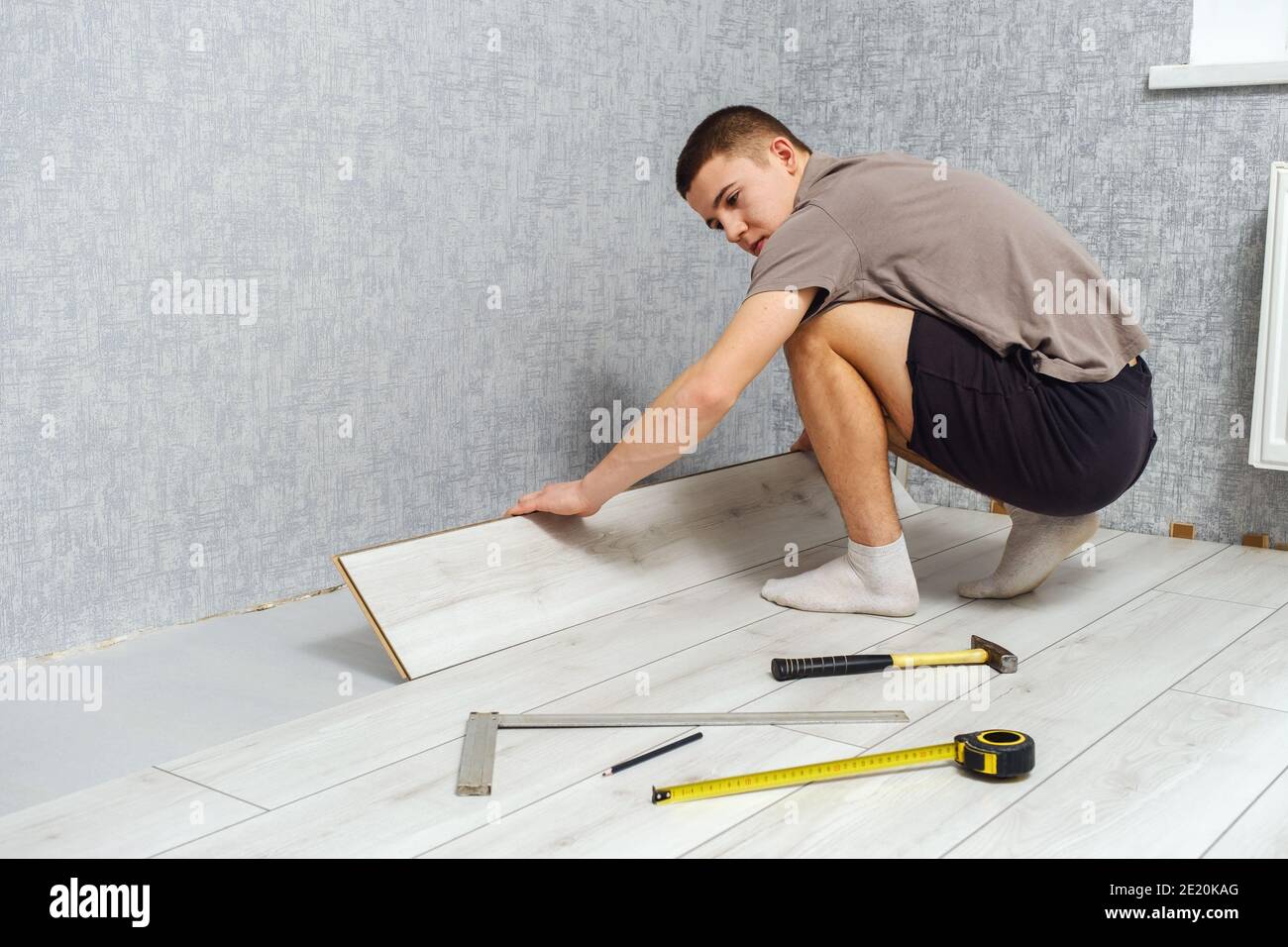 Il giovane uomo sta mettendo un pannello di legno di pavimento laminato all'interno. Foto Stock