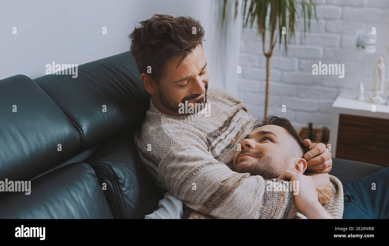 Felice coppia omosessuale maschile newlywed che passa tempo di qualità insieme, coccolarsi e rilassarsi sul divano. Foto di alta qualità Foto Stock