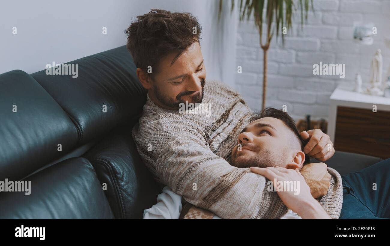 Felice coppia omosessuale maschile trascorrere del tempo di qualità insieme, coccolarsi e rilassarsi sul divano. Foto di alta qualità Foto Stock