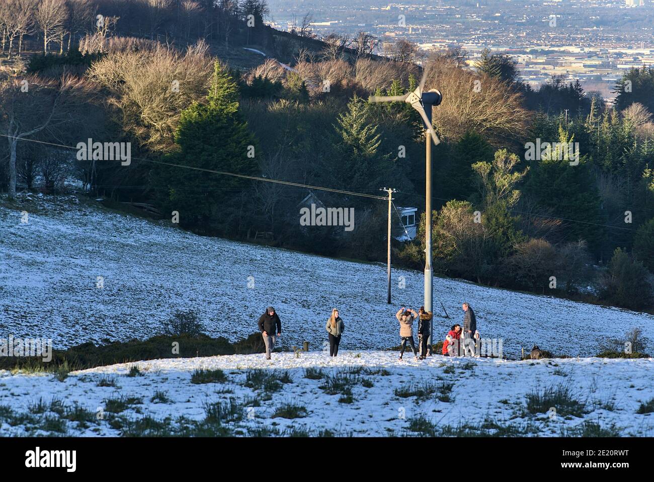 Persone che giocano a giochi di neve all'aperto e che fanno attività accanto alla turbina eolica a Dublin Panoramic View Point, Killakee, Co. Dublino, Irlanda. Inverno irlandese Foto Stock