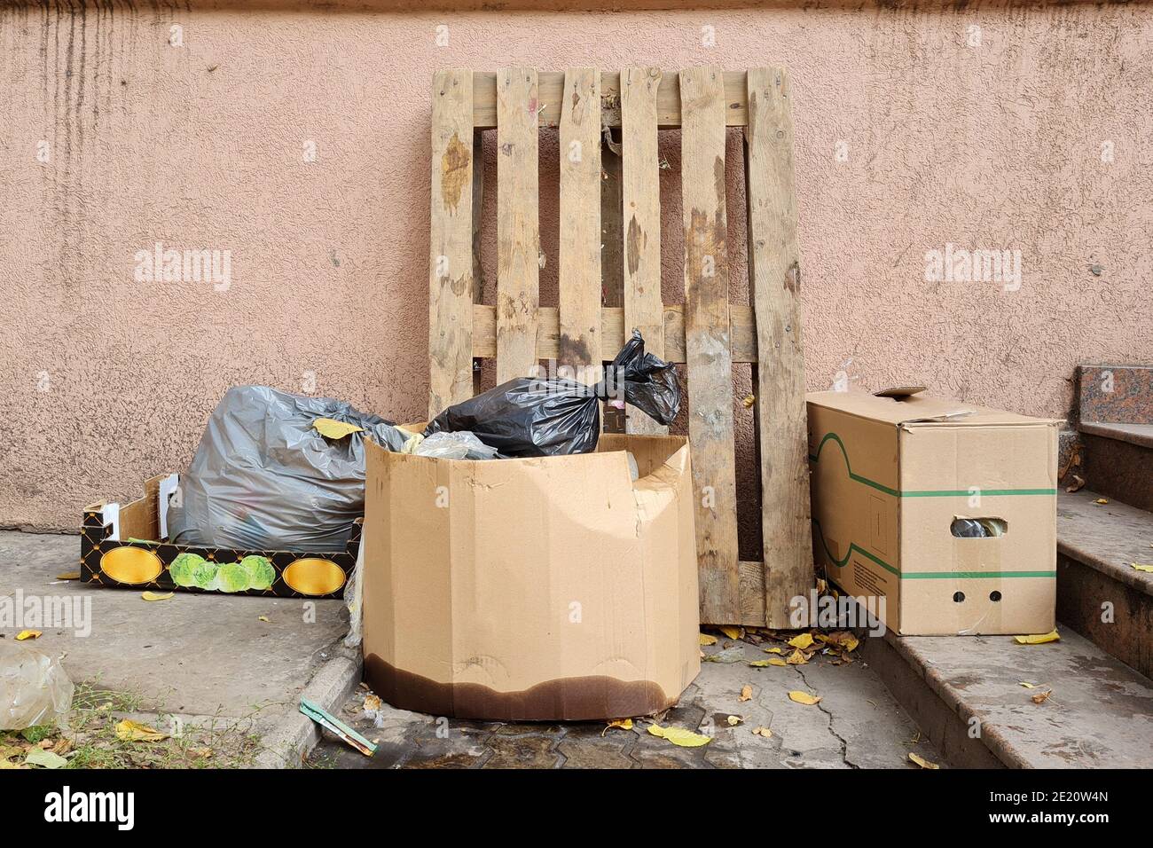 Pallet di legno e spazzatura in sacchi di plastica e scatole di carta vicino a un muro di costruzione su una strada della città. Foto Stock