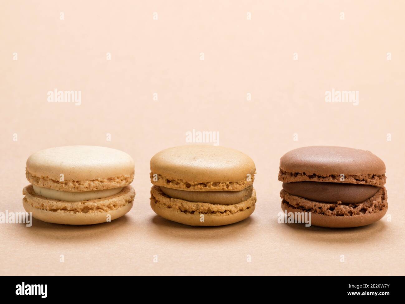 Primo piano di pasta di macaron ripiena di vaniglia, caffè e salsa al cioccolato su fondo marrone chiaro Foto Stock