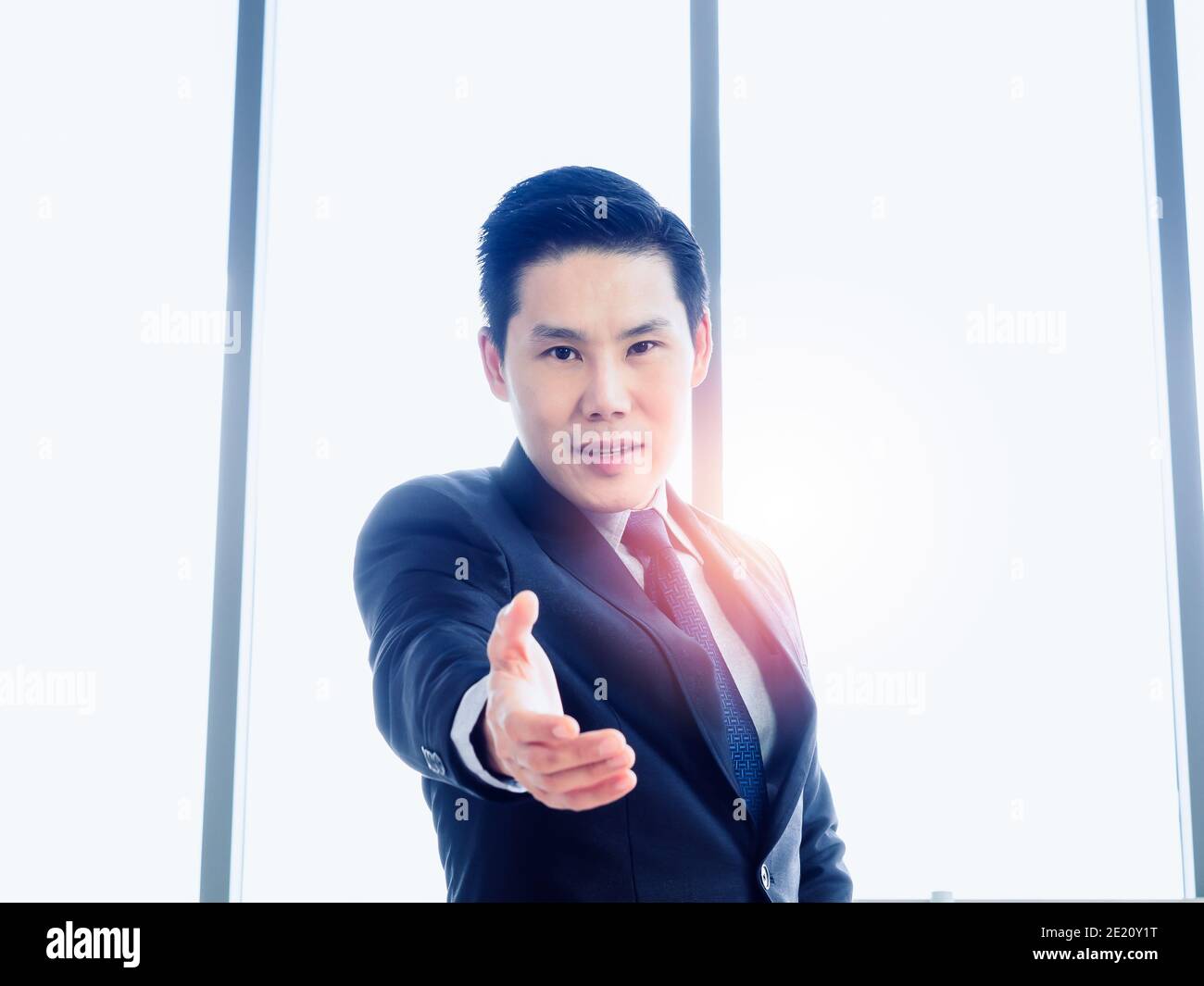 Bell'uomo d'affari asiatico con una mano aperta pronta per sigillare un affare su sfondo enorme finestra di vetro. L'uomo d'affari in vestito tiene fuori la mano che aspetta f Foto Stock