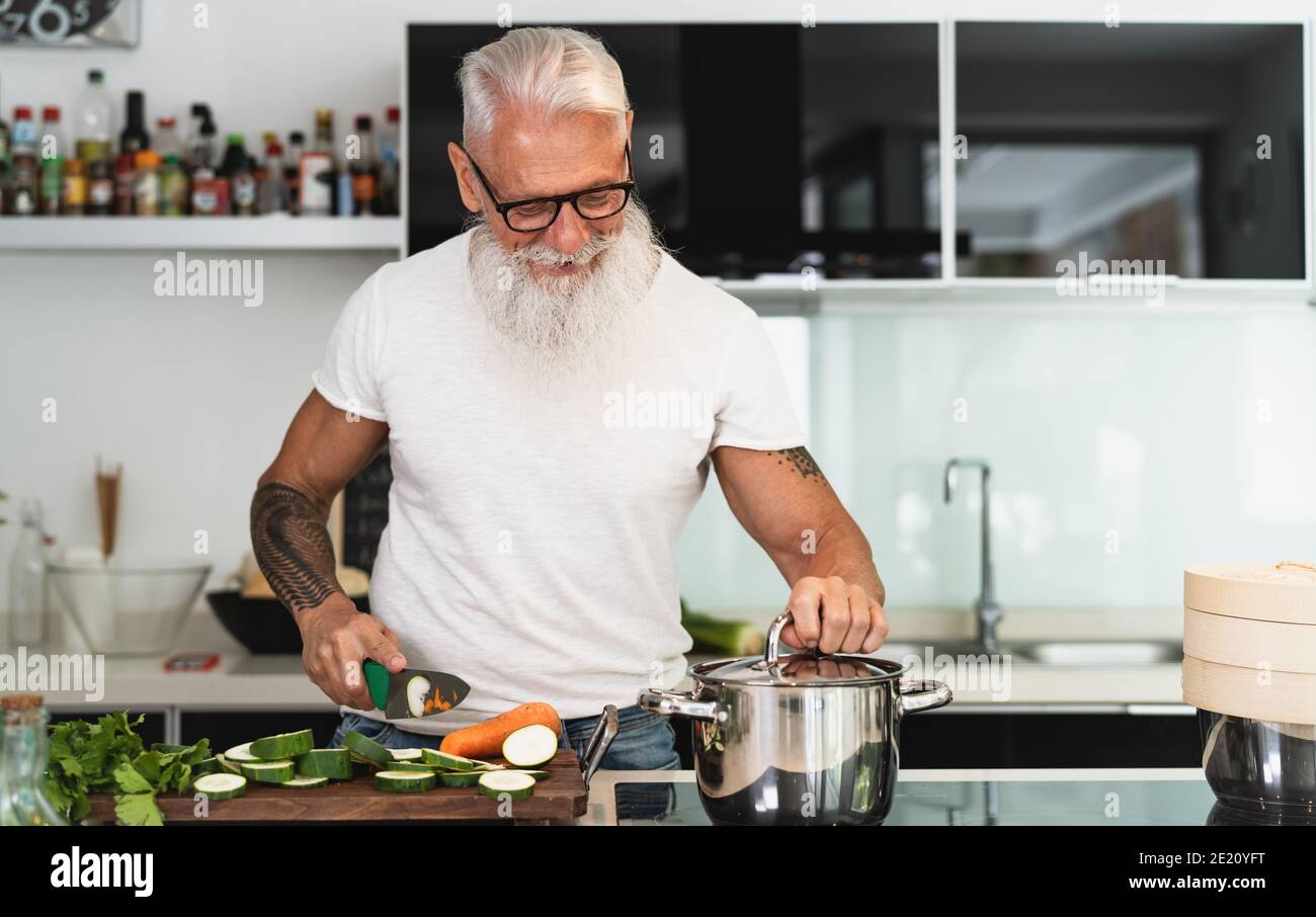 Felice uomo anziano che si diverte a cucinare a casa - anziani persona che prepara il pranzo di salute in cucina moderna Foto Stock