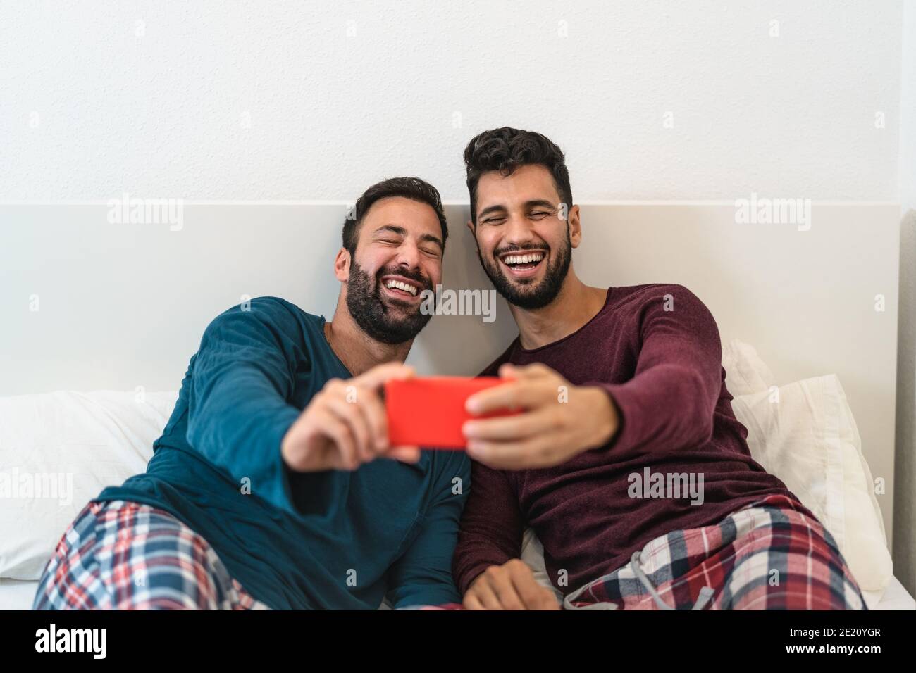 Felice coppia gay divertirsi utilizzando smartphone mobile a letto - amore omosessuale e concetto di tecnologia Foto Stock