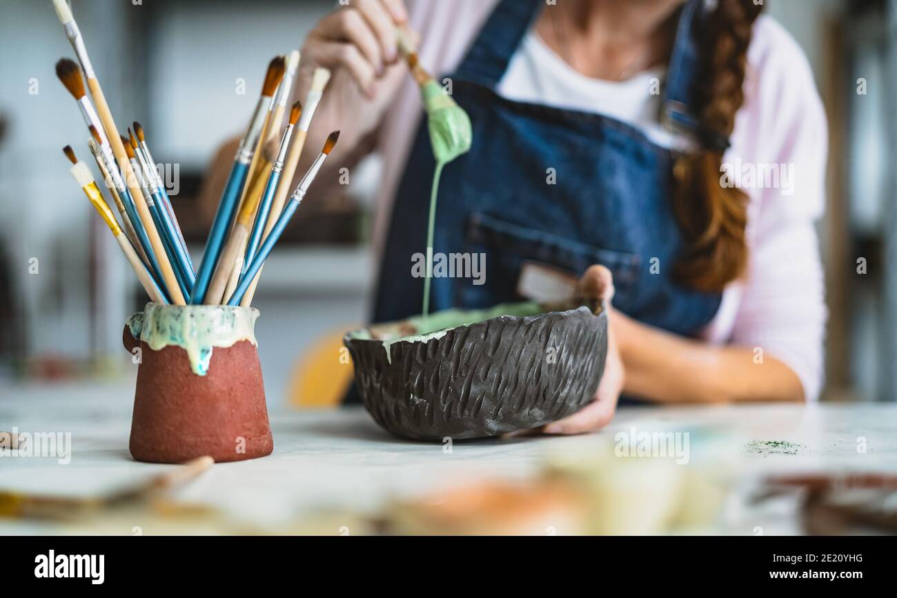 Donna che mescola vernice con pennello all'interno della ciotola in ceramica in officina studio - opere d'arte e concetto di artigianato creativo Foto Stock