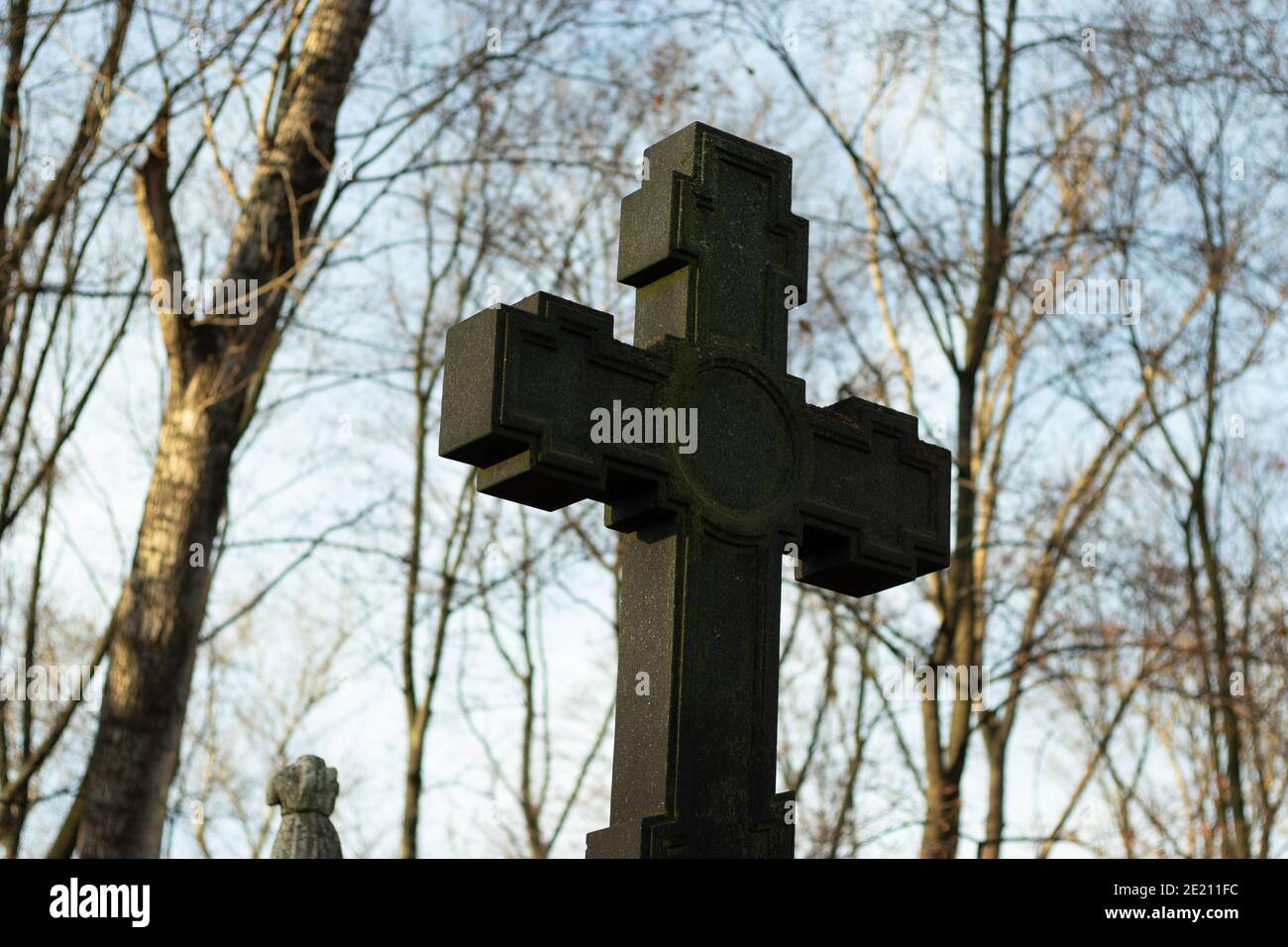 Grande croce cristiana fatta di pietra scura sullo sfondo di rami di albero e cielo. Concetto di religione. Foto Stock